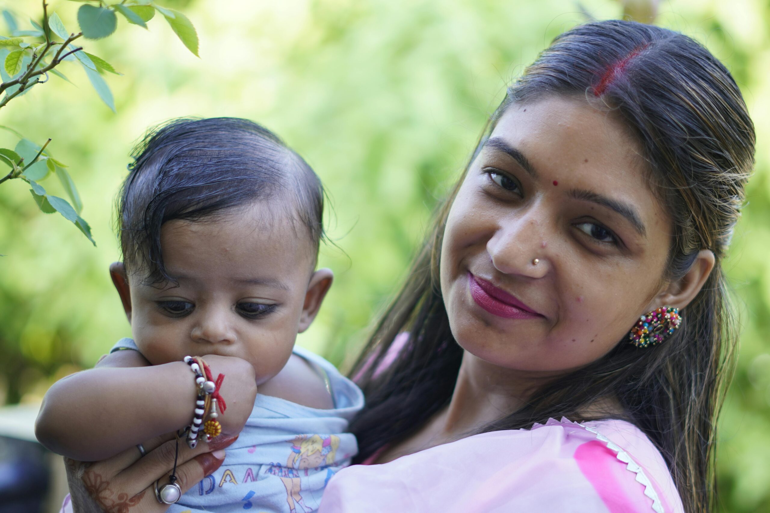 A loving mother holding her baby outdoors, showcasing happiness and cultural attire in a summer setting.